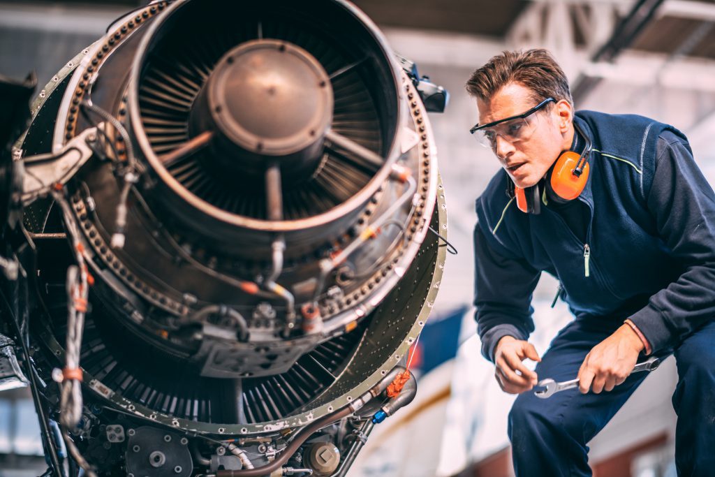 Aircraft mechanic in a hangar holding a wrench while repairing and maintaining a small airplane's jet engine